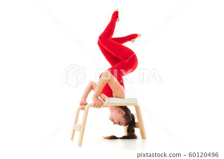 Attractive brunette girl in a red tracksuit wishes gymnastic exercises upside down on a white Attractive brunette girl in a red tracksuit wishes gymnastic exercises upside down on a white 60120496