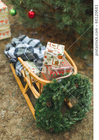 Beatiful wooden Santa's sledge with Christmas gifts and wreath, over the background of winter forest and decorated Christmas tree. Merry Christmas and Happy New Year Concept. 60120681