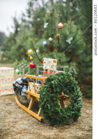 Beatiful wooden Santa's sledge with Christmas gifts and wreath, over the background of winter forest and decorated Christmas tree. Merry Christmas and Happy New Year Concept. 60120683