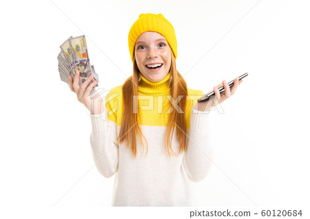 european attractive red-haired girl holding money with a phone in her hands on a white background 60120684