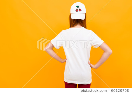 smiling european red-haired girl in a white t-shirt stands with her back on a yellow background. smiling european red-haired girl in a white t-shirt stands with her back on a yellow background. 60120708