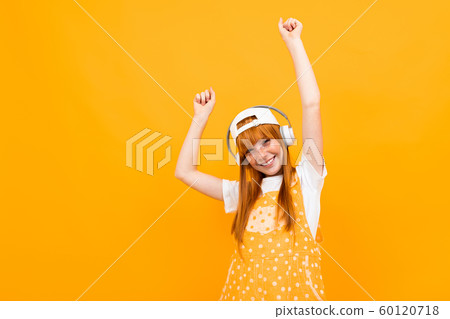 portrait of a european red-haired girl comes off to music on a yellow background. 60120718