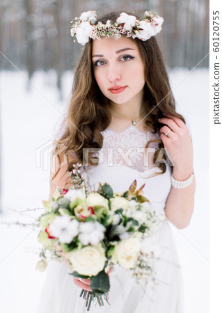 stylish bride in a beautiful dress, wedding in winter, floristry for the wedding, bouquet and wreath on head. girl with long curly hair stylish bride in a beautiful dress, wedding in winter, floristry for the wedding, bouquet and wreath on head. girl with long curly hair 60120755
