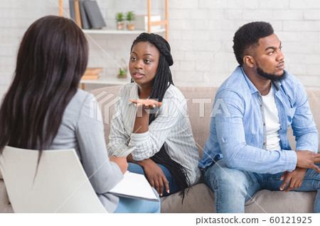 Wife Sitting Next To Her Displeased Husband And Talking To Counselor Wife Sitting Next To Her Displeased Husband And Talking To Counselor 60121925