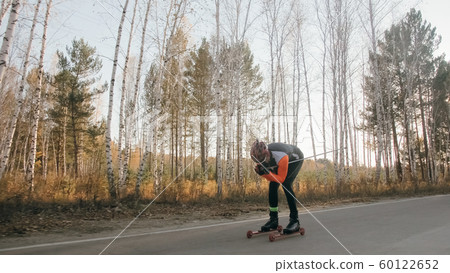 Training an athlete on the roller skaters. Biathlon ride on the roller skis with ski poles, in the helmet. Autumn workout. Roller sport. Training an athlete on the roller skaters. Biathlon ride on the roller skis with ski poles, in the helmet. Autumn workout. Roller sport. 60122652