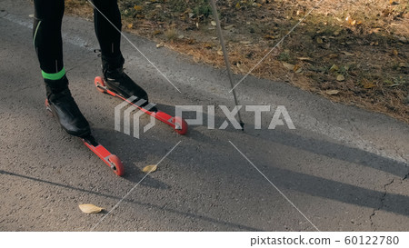 Training an athlete on the roller skaters. Biathlon ride on the roller skis with ski poles, in the helmet. Autumn workout. Roller sport. Athlete is getting ready to start. Training an athlete on the roller skaters. Biathlon ride on the roller skis with ski poles, in the helmet. Autumn workout. Roller sport. Athlete is getting ready to start. 60122780