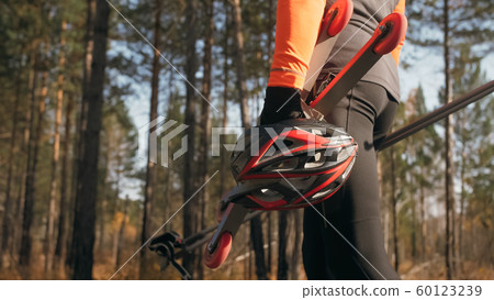 Training an athlete on the roller skaters. Biathlon ride on the roller skis with ski poles, in the helmet. Autumn workout. Roller sport. The athlete goes and holds sports equipment in his hand. Training an athlete on the roller skaters. Biathlon ride on the roller skis with ski poles, in the helmet. Autumn workout. Roller sport. The athlete goes and holds sports equipment in his hand. 60123239