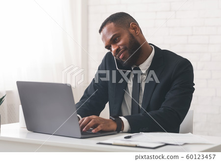 Cheerful businessman talking to client by phone and using computer 60123457