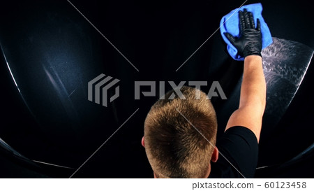 Using rag in palm of your hand, drops are removed from the car. Drop flow down the hood. Close up view of bonnet car. Polishing and washing auto. 60123458