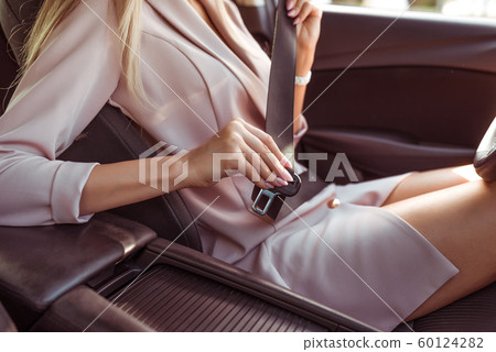 Close-up, woman in car interior, fastens seat belt. Traffic safety on road in city, activation of airbags. Pink business suit girl. Close-up, woman in car interior, fastens seat belt. Traffic safety on road in city, activation of airbags. Pink business suit girl. 60124282