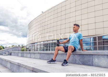 sports man resting after hard workout, shaker with protein and water, a daytime workout in city, active lifestyle, modern fitness workout. Free space. 60125015