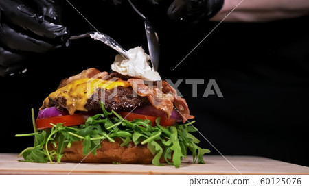 Craft burger is cooking on black background. Consist: sauce, arugula, tomato, onion, bacon, currant sauce, ricotta cheese, air bun and marble meat. Craft burger is cooking on black background. Consist: sauce, arugula, tomato, onion, bacon, currant sauce, ricotta cheese, air bun and marble meat. 60125076