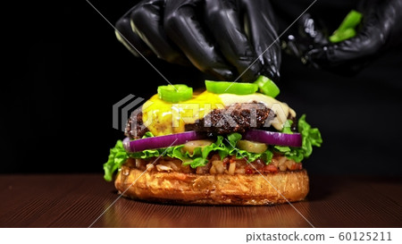 Craft burger is cooking on black background. Consist: sauce salsa, lettuce, red onion, pickle, cheese, chilli green pepper, bun, marbled meat beef. Craft burger is cooking on black background. Consist: sauce salsa, lettuce, red onion, pickle, cheese, chilli green pepper, bun, marbled meat beef. 60125211