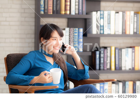 Beautiful portrait young asian woman smiling using mobile smart phone talking enjoy and drink coffee Beautiful portrait young asian woman smiling using mobile smart phone talking enjoy and drink coffee 60129980