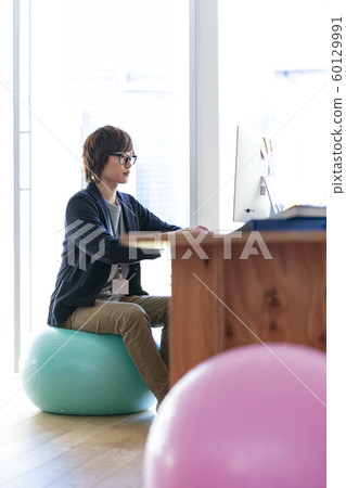 Young man sitting on balance ball and going to computer Young man sitting on balance ball and going to computer 60129991