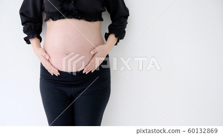 Pregnant woman in black dress and hands hold on belly on a white wall background 60132869
