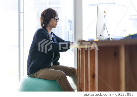 Young man sitting on balance ball and going to computer 60133095