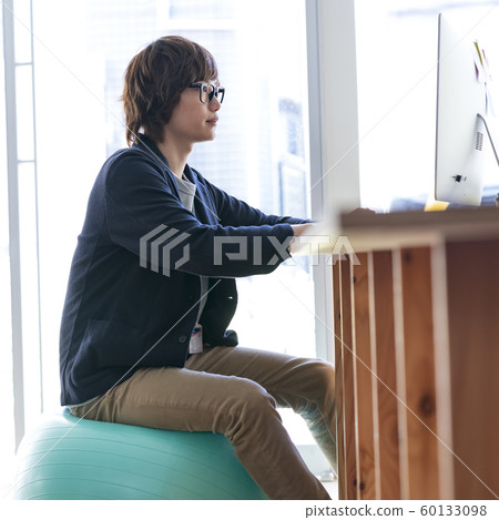 Young man sitting on balance ball and going to computer 60133098