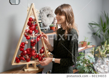 Alternative wooden christmas tree in womans hands . A handmade Christmas tree and red christmas balls. Alternative wooden christmas tree in womans hands . A handmade Christmas tree and red christmas balls. 60134833