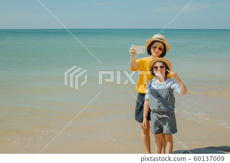 Woman and child standing and taking selfie with smartphone on sand beach. Woman and child standing and taking selfie with smartphone on sand beach. 60137009