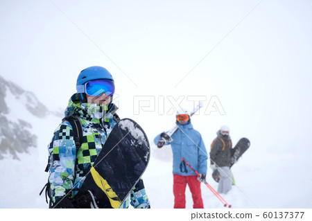 Photo of three sports people with skis and snowboard walking through winter resort Photo of three sports people with skis and snowboard walking through winter resort 60137377