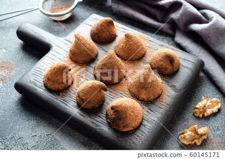 Delicious chocolate truffles sprinkled with cocoa powder and walnuts on a wooden stand. Dark concrete background. 60145171