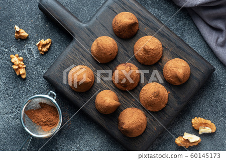 Delicious chocolate truffles sprinkled with cocoa powder and walnuts on a wooden stand. Dark concrete background. Copy space. 60145173
