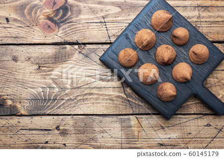 Delicious chocolate truffles sprinkled with cocoa powder on a wooden stand. Wooden background. Copy space. 60145179