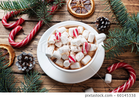 A Cup of hot chocolate with marshmallows. Christmas tree and decorations, cane caramel and oranges nuts Wooden background 60145338