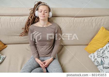 Peaceful young woman with headphones listening to meditation music on couch 60145853
