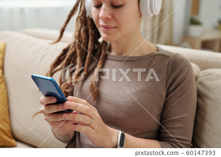 Hands of young woman with headphones scrolling in smartphone for music Hands of young woman with headphones scrolling in smartphone for music 60147393