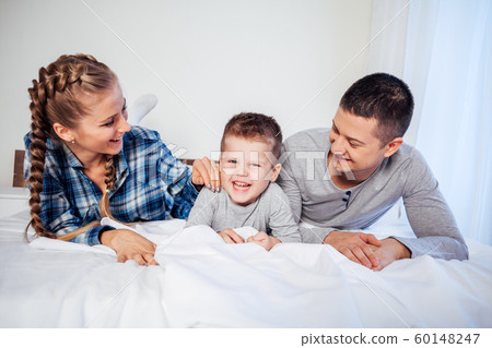 mom dad and son in the morning lying on the bed at home 60148247