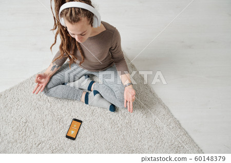 View of serene young woman in headphones sitting in pose of lotus 60148379