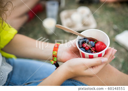 Unrecognizable woman at summer festival, sitting on the ground and eating fruit. 60148551
