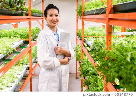 Young successful female researcher or agronomist in whitecoat standing in aisle Young successful female researcher or agronomist in whitecoat standing in aisle 60148770
