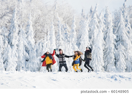 A group of young friends on a walk outdoors in snow in winter forest. 60148905