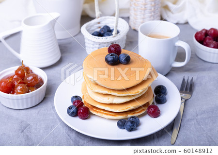 Pancakes with blueberries, cherries and mini apple jam. A cup of coffee and gravy boat in the background. Traditional american pancakes. Close-up. Pancakes with blueberries, cherries and mini apple jam. A cup of coffee and gravy boat in the background. Traditional american pancakes. Close-up. 60148912