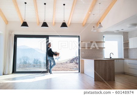 Mature man with moving box standing by patio door in unfurnished house. 60148974