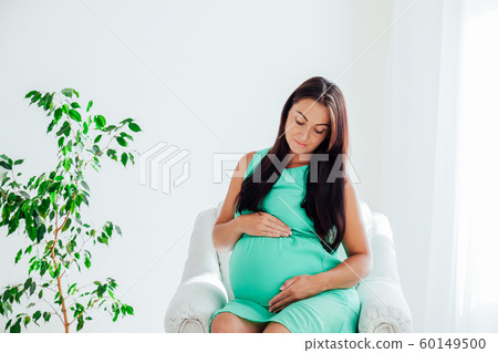 a pregnant woman before childbirth sits in white couch 60149500