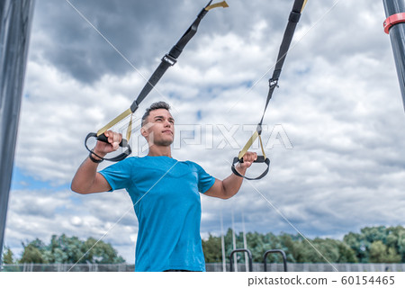Male athlete, pulls himself on hinges, push-ups on elastic bands trx strap, in summer in city. Fitness motivation youth lifestyle. Free space for copy text. Sportswear T-shirt. Male athlete, pulls himself on hinges, push-ups on elastic bands trx strap, in summer in city. Fitness motivation youth lifestyle. Free space for copy text. Sportswear T-shirt. 60154465