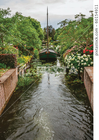 Canal with decorative boat next a flowery garden at Drimmelen Canal with decorative boat next a flowery garden at Drimmelen 60154911