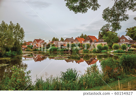 Canal next to rustic houses with bushes and trees Canal next to rustic houses with bushes and trees 60154927