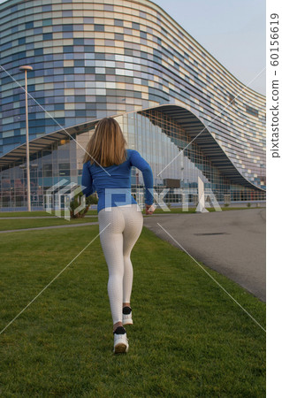 Young female runner in hoody is jogging in the city street. View from the back. 60156619