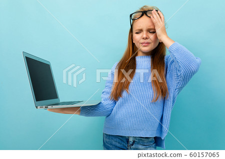 tired european girl holding a computer on a light blue wall 60157065