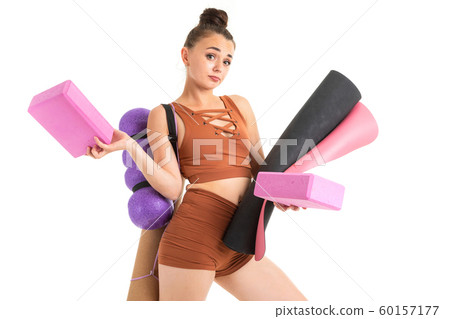 European brunette girl dressed in a brown sports top and shorts holds sports paraphernalia for yoga European brunette girl dressed in a brown sports top and shorts holds sports paraphernalia for yoga 60157177