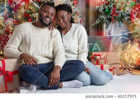 Portrait of romantic black couple sitting on floor near Xmas tree Portrait of romantic black couple sitting on floor near Xmas tree 60157971