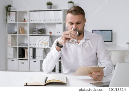 Busy mature head of business company drinking water while using touchpad Busy mature head of business company drinking water while using touchpad 60158814