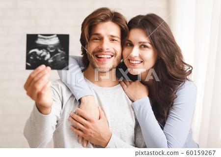 Happy millennial couple holding ultrasound scan of their expecting baby Happy millennial couple holding ultrasound scan of their expecting baby 60159267