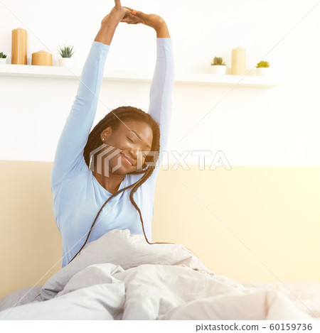 Happy Black Girl Waking Up Stretching Arms Sitting In Bedroom 60159736