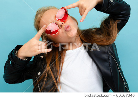 attractive european girl in a leather jacket in sunglasses shows a class on a light blue background attractive european girl in a leather jacket in sunglasses shows a class on a light blue background 60167346